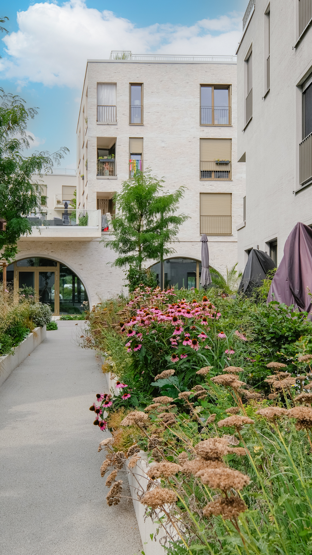 ulp_ek_fo_freianalgen A2 A3_web_aug25-35 Foto vom Neubau Spöttinger Höfe mit markanten Rundbogenfenstern im Erdgeschoss und Blumenbeet im Vordergrund.