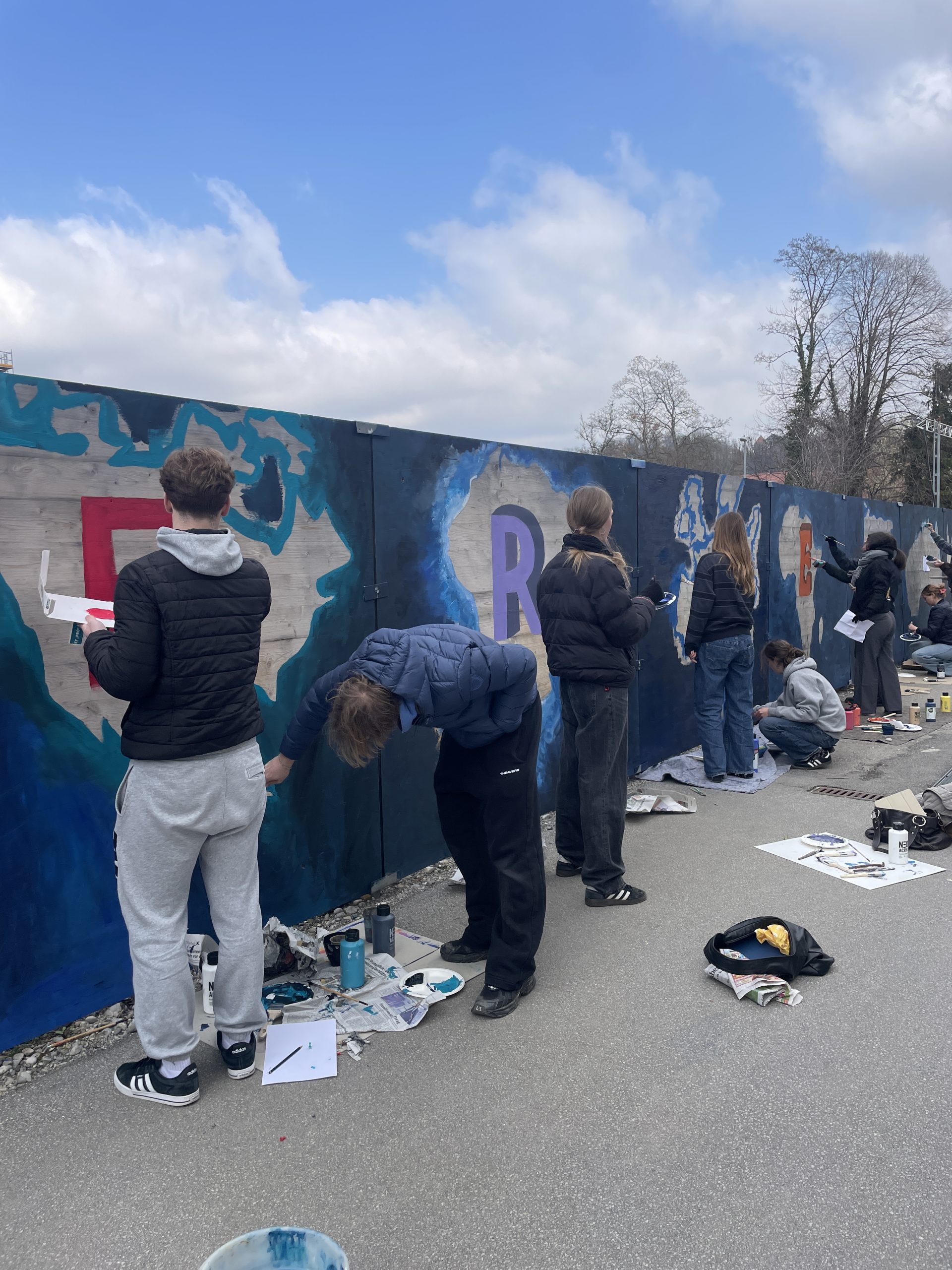 Mehrere Personen gestalten mit Farbe einen Bauzaun